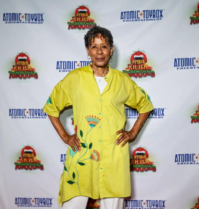 A guest in a bright yellow embroidered tunic posing with hands on hips against the step-and-repeat.