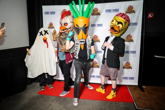 Four costumed puppet characters, including a carrot and a ghost, lined up on the red carpet.
