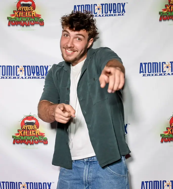 A guest in a green overshirt pointing both hands at the camera on the red carpet.