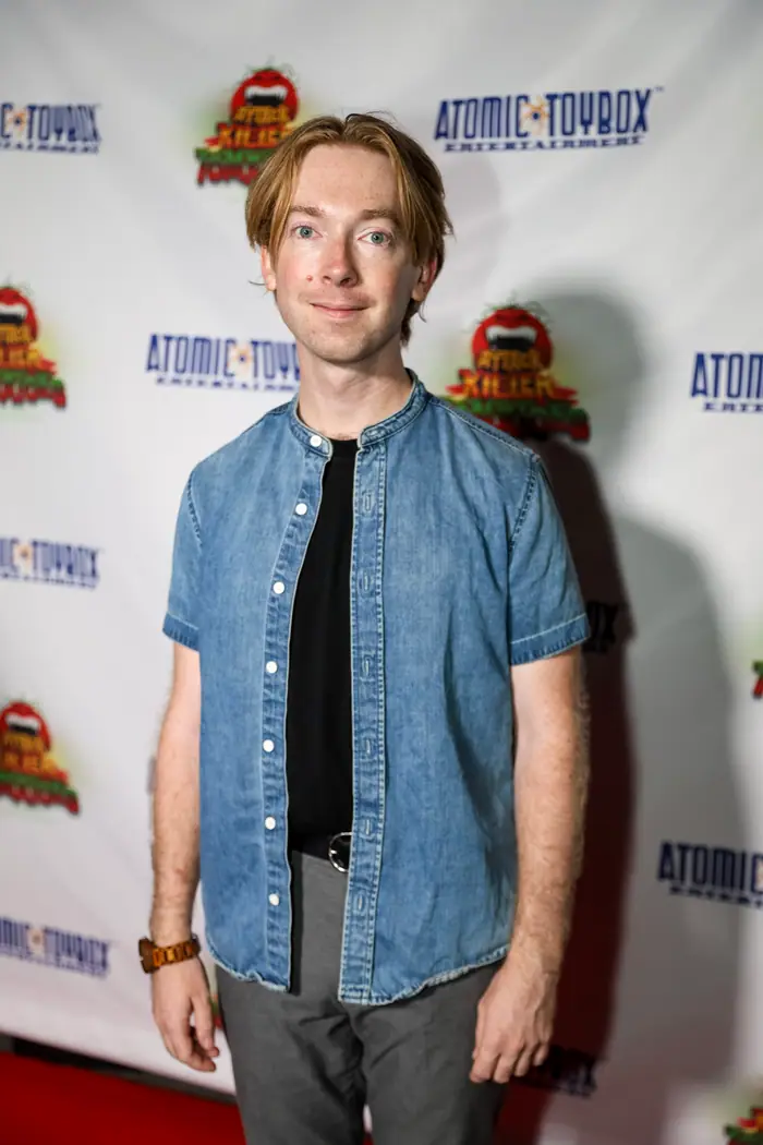 A guest in a short-sleeved denim shirt standing on the red carpet.