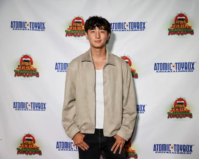 A guest in a cream jacket and black trousers posing against the step-and-repeat.