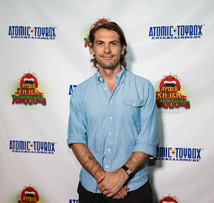 A guest in a light blue shirt standing with hands clasped in front of the step-and-repeat.